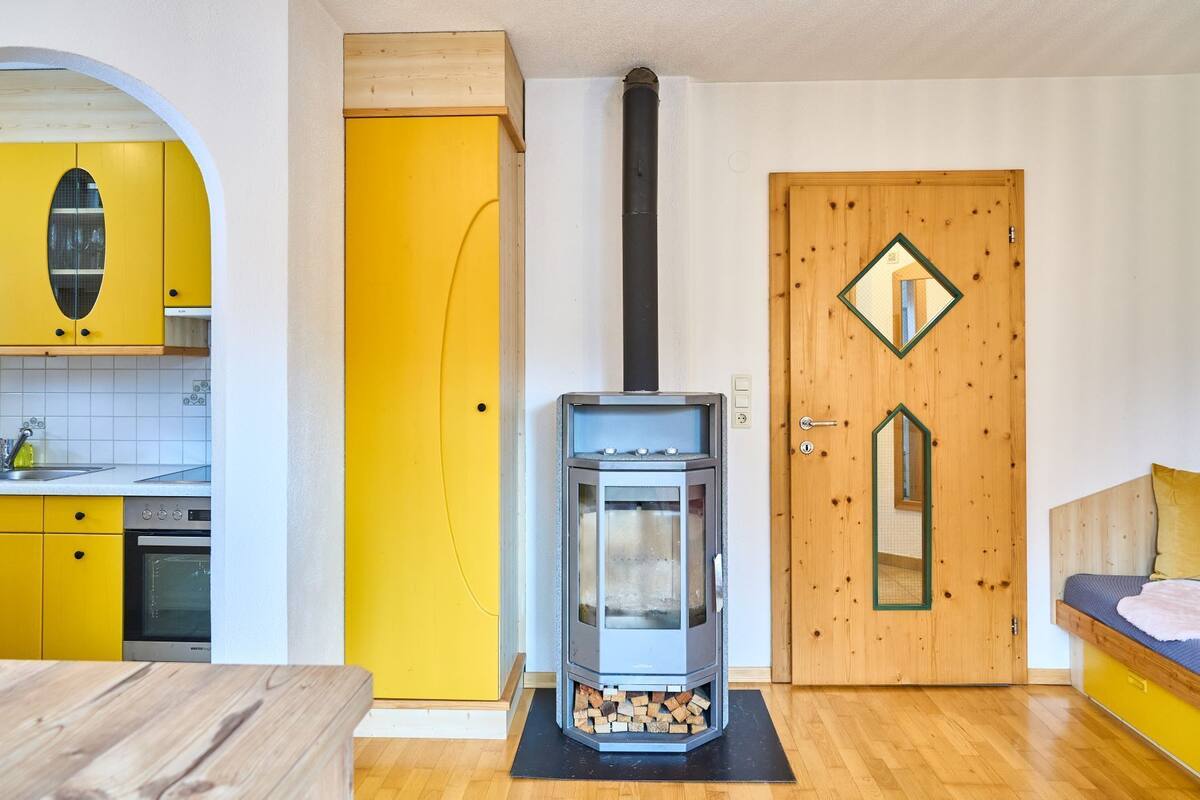 A compact kitchen with yellow cabinets, a built-in oven, and a wood-burning stove.