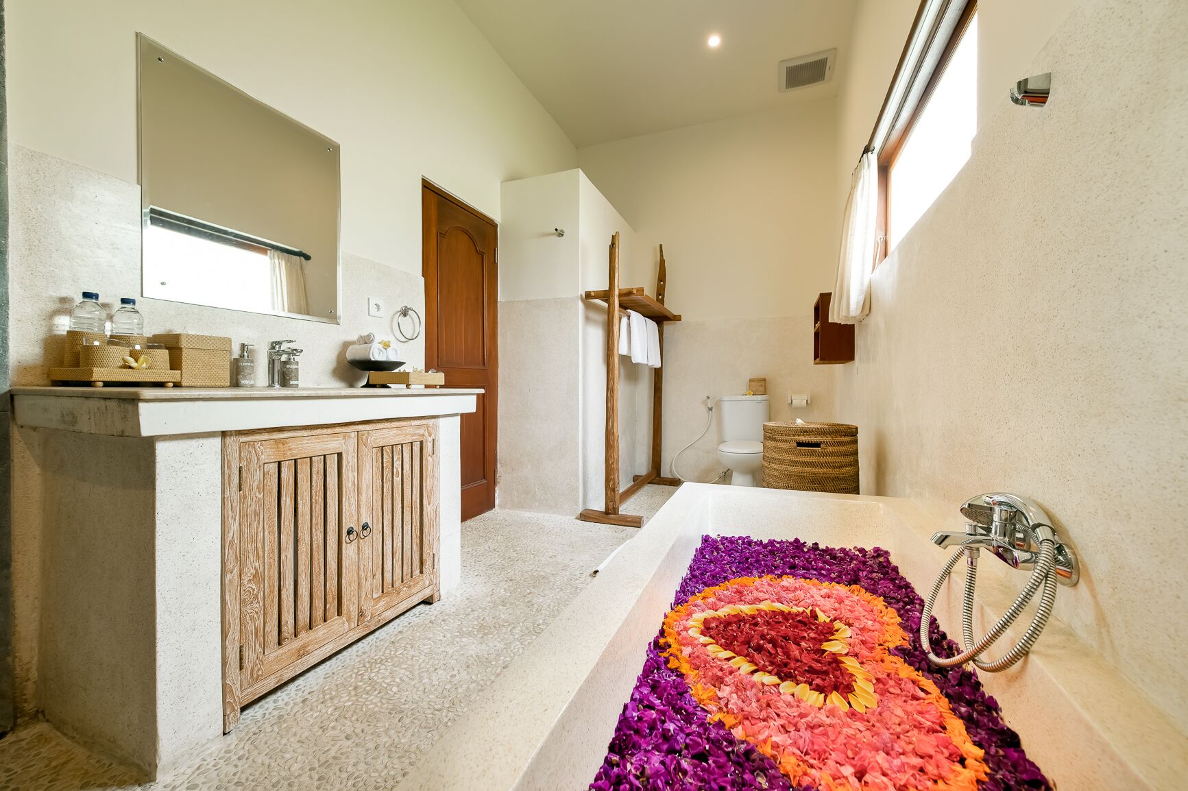 A bathroom with a wooden vanity, a large bathtub with a colorful flower arrangement, and a shower area.