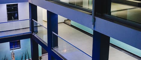 Ein mehrstöckiges Gebäude mit einem zentralen Atrium, Glasgeländern und einem Poolbereich.