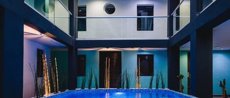 A modern indoor swimming pool with glass railings and a tiered ceiling.