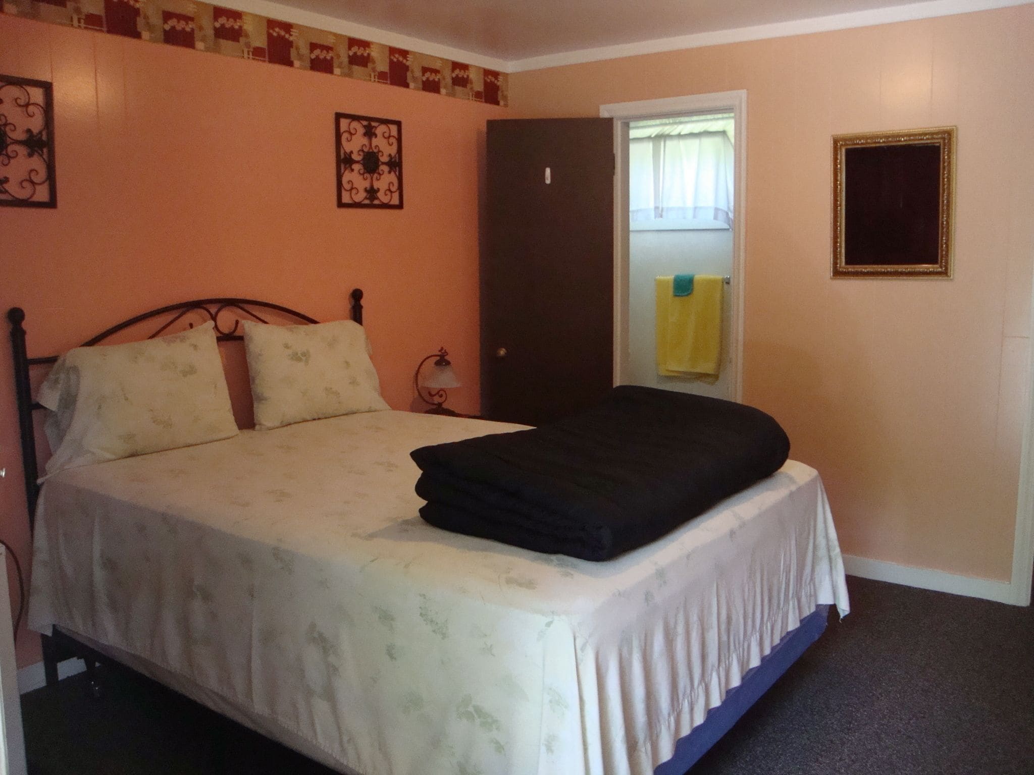 A bedroom with a bed, a door, a window, and a wall-mounted picture frame.