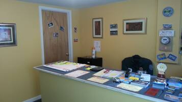 A reception desk with various informational materials, a door, and a wall with framed pictures and a no credit card payment sign.