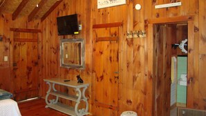 A wooden cabin interior with a television mounted on the wall, a small table, and a door leading to a bathroom. - Paradise Resort and Cabins (Gansevoort)