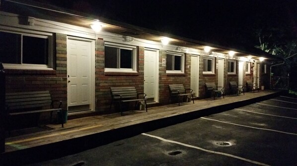 A row of single-story motel rooms with individual doors and windows, a covered outdoor seating area with benches, and a parking lot. - Paradise Resort and Cabins (Gansevoort)