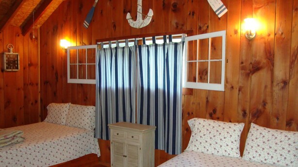 A wooden cabin room with two beds, a dresser, and a large window with curtains. - Paradise Resort and Cabins (Gansevoort)
