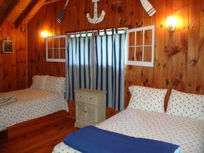 A wooden cabin room with two beds, a dresser, and a large window with curtains. - Paradise Resort and Cabins (Gansevoort)