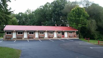 A motel with a red roof and brick exterior, featuring a parking lot and a small garden area.
