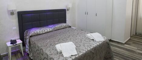 A bedroom with a bed, a nightstand with a phone, a wardrobe, and a mirror.