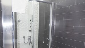 En modern dusch med en glasdörr, en vit handduk hängande på dörren och en kontrollpanel med flera vred.