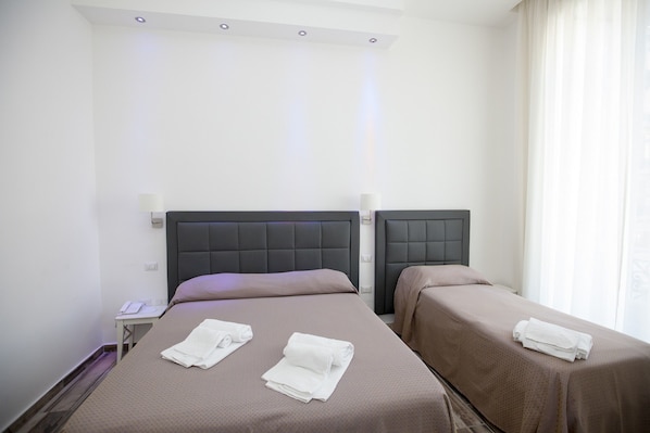 A hotel room with two beds, each with a headboard and a bedside table. - Napoli Garibaldi Square (Naples)