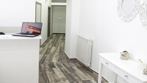 Ett modernt hotellrum med ett vitt skrivbord, en bärbar dator, ett element och en spegel.