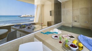 A balcony with a view of the ocean, a glass shower enclosure, and a table with fruits and drinks. - White Bay Resort (Syracuse)
