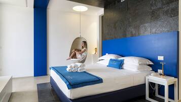 A modern bedroom with a hanging chair, a neatly made bed with blue bedding, and a blue accent wall.