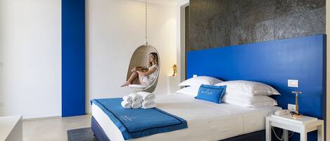 A modern bedroom with a hanging chair, a neatly made bed with blue bedding, and a blue accent wall.