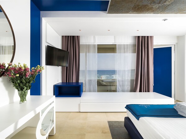 A modern hotel room with a bed, a TV, a desk, and a view of the sea. - White Bay Resort (Syracuse)
