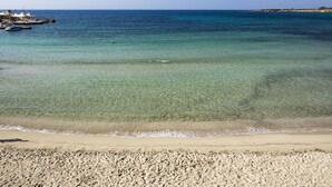 A beach with clear shallow waters, a sandy shore, and a distant pier with buildings. - White Bay Resort (Syracuse)
