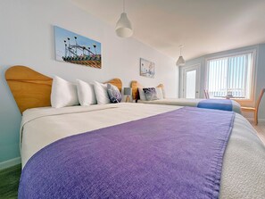 A hotel room with a large bed, a headboard, a window with blinds, and artwork on the walls.