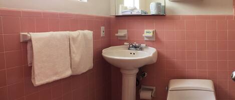 A bathroom with pink tiles, a pedestal sink, a toilet, and a window.