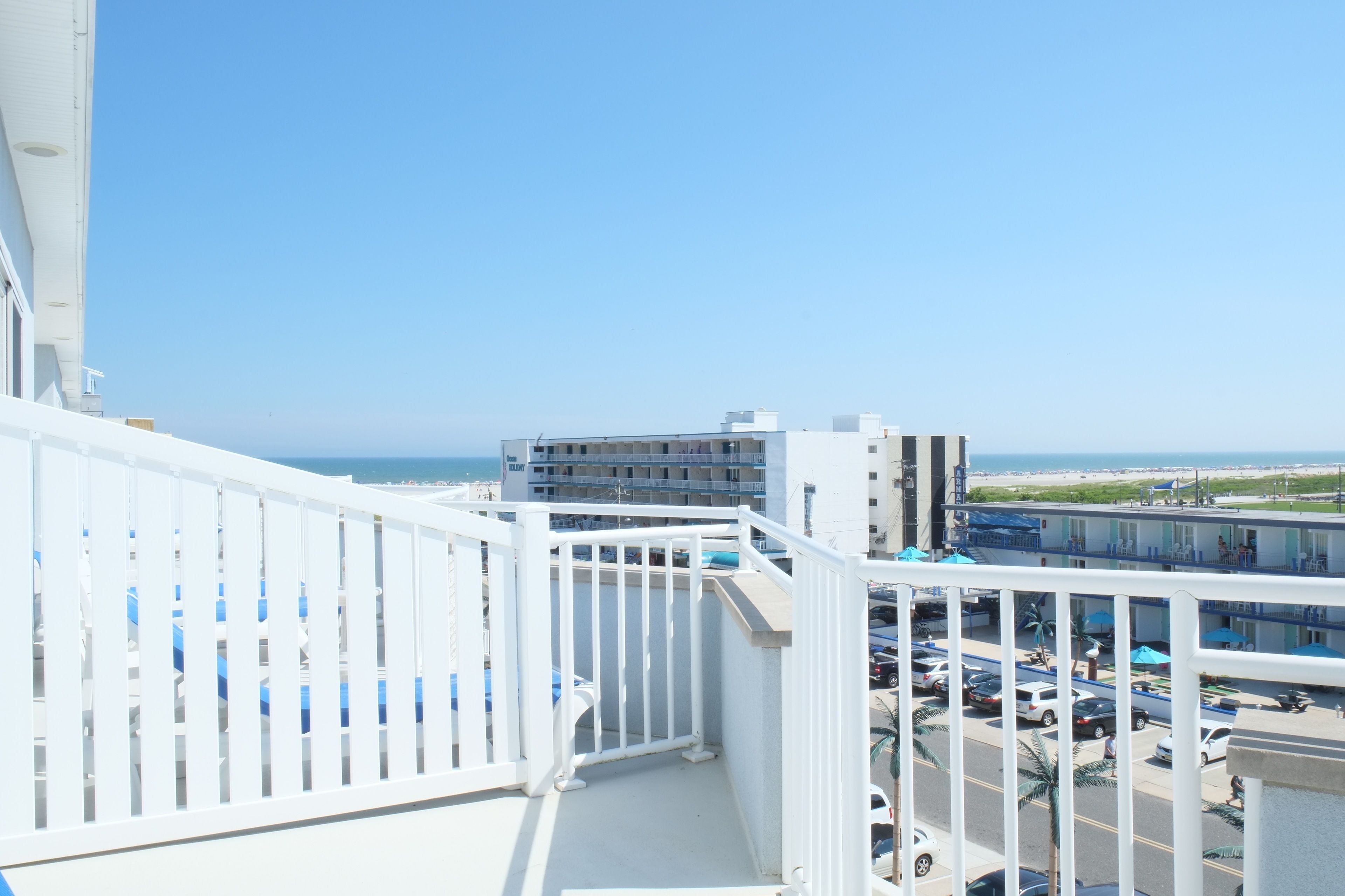A balcony with a white railing overlooking a parking area and buildings.