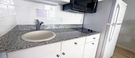 Een keuken met witte kasten, een granieten aanrecht, een spoelbak, een zwarte magnetron en een witte koelkast.