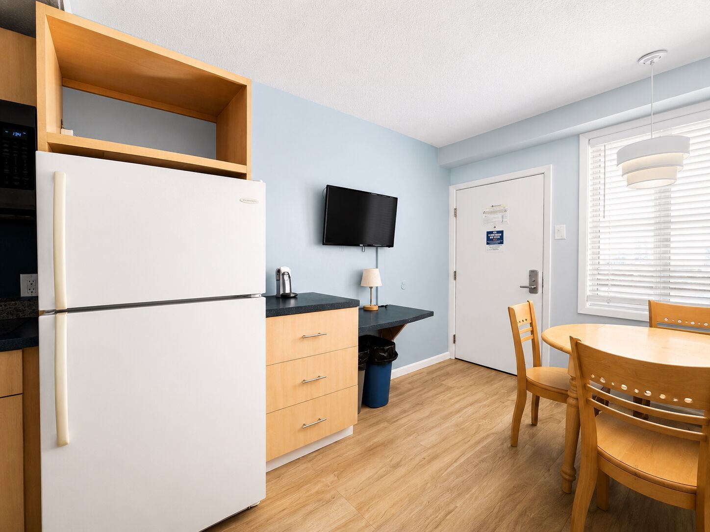 A compact kitchen with a refrigerator, a microwave, a sink, a wooden table, and a chair.