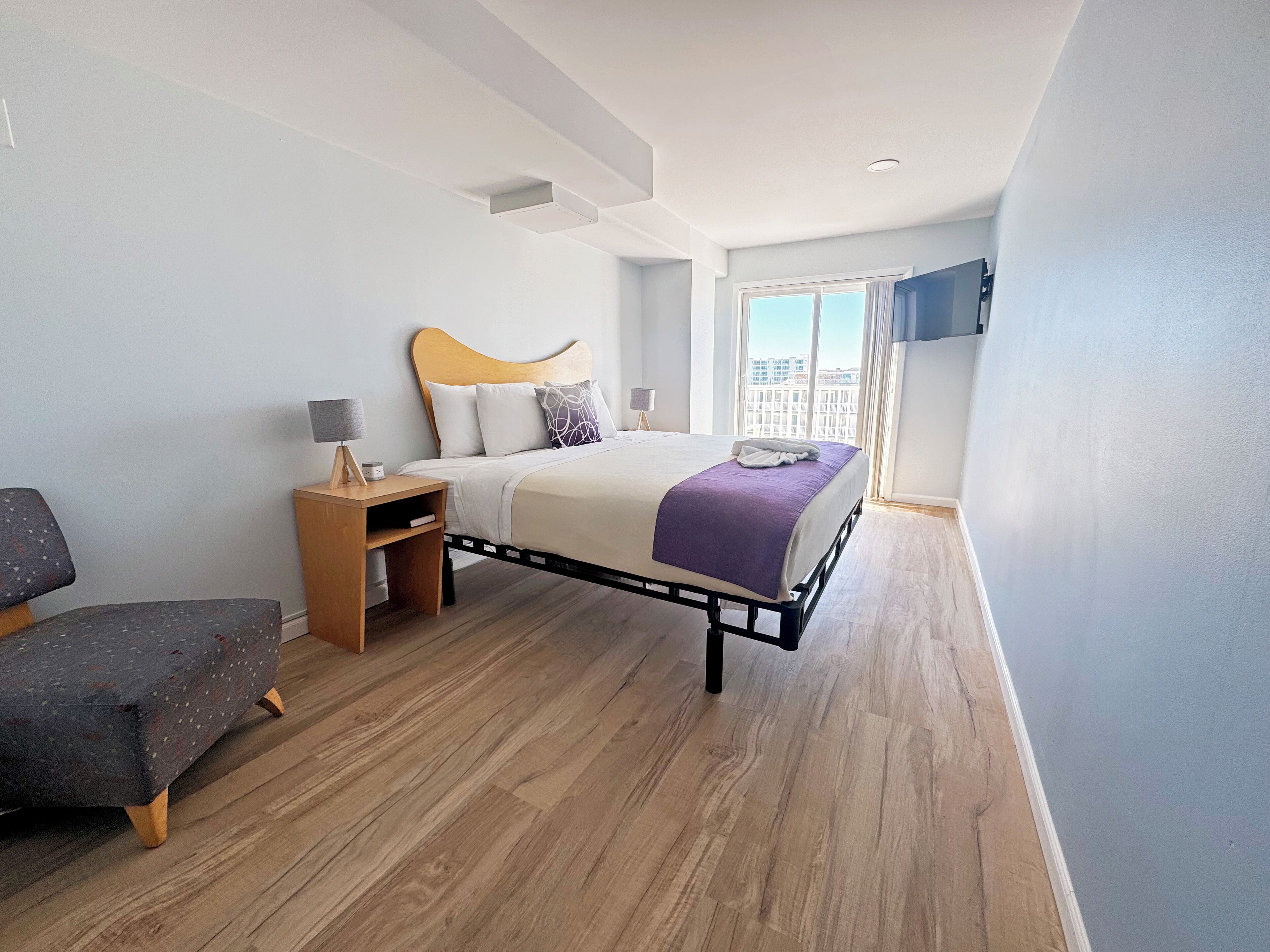 Un dormitorio moderno con cama, mesitas de noche, un banco y un ventanal grande.