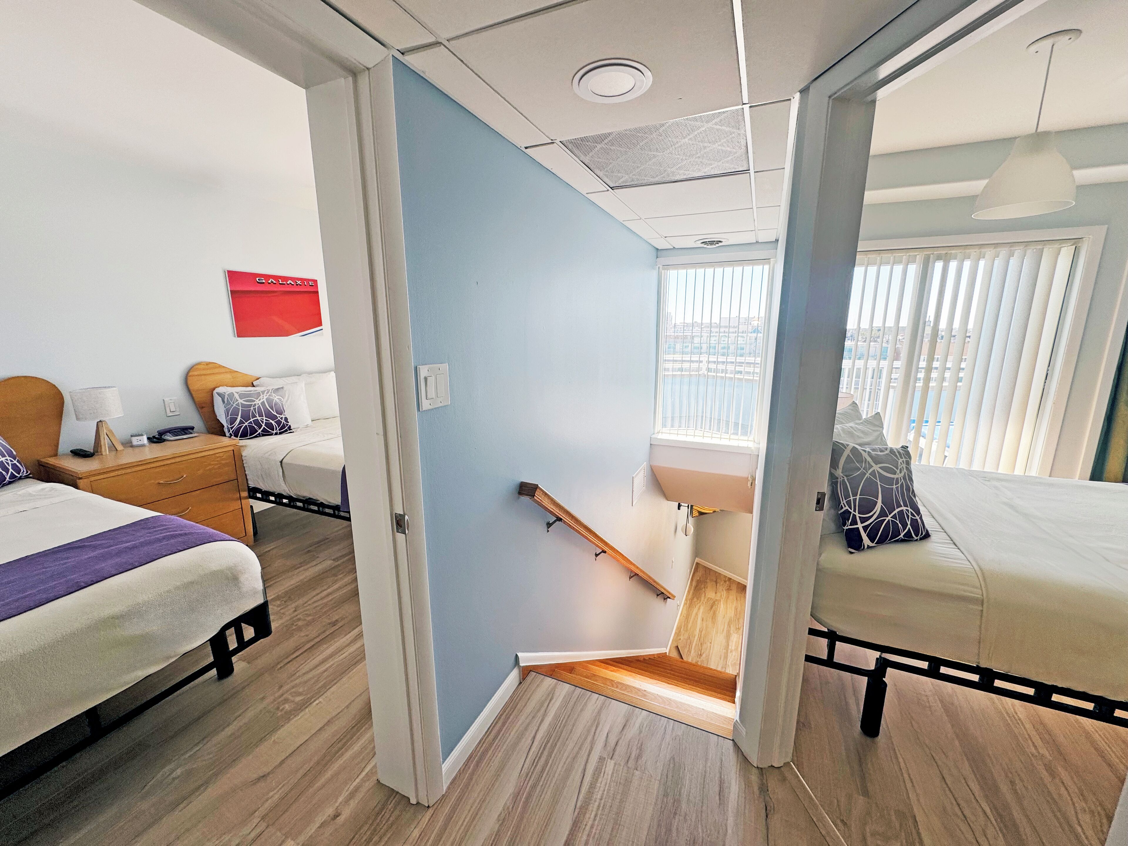 Une chambre d’hôtel avec deux lits, un plancher en bois, un mur d’accent bleu et une fenêtre avec des stores.