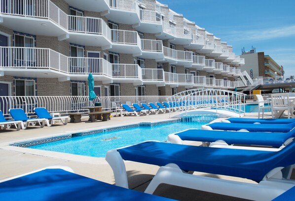 A hotel pool area with multiple levels of balconies, lounge chairs, and a swimming pool.
