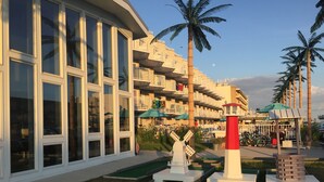 A hotel with a modern design, featuring large windows and balconies. There are palm trees and a miniature golf course with windmills. - Shalimar Resort (Wildwood Crest)