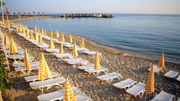 A beach with rows of sun loungers and yellow and white striped umbrellas. - Incekum Su Hotel (Alanya)