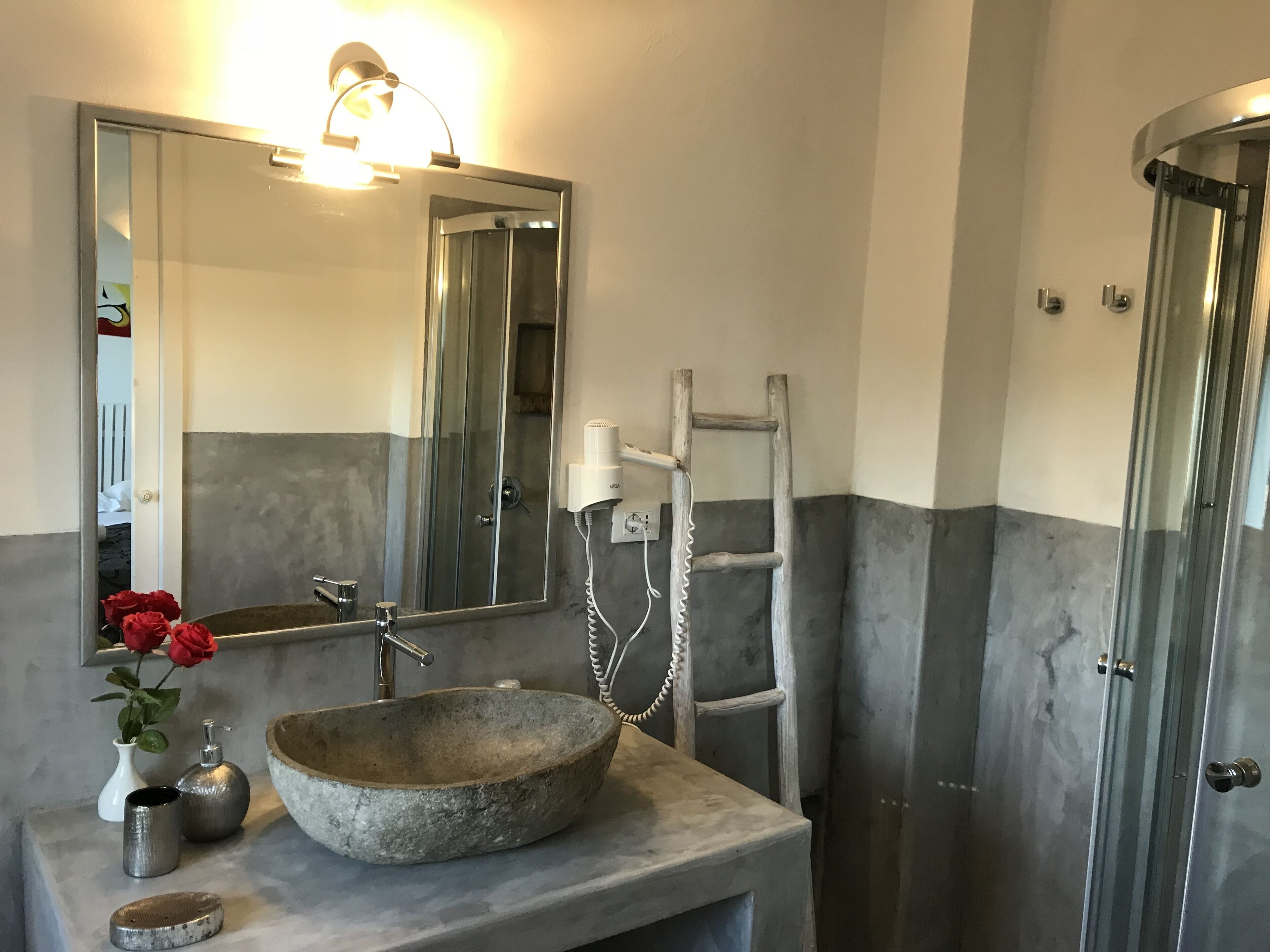 A bathroom with a stone sink, a mirror, a towel rack, and a shower door.