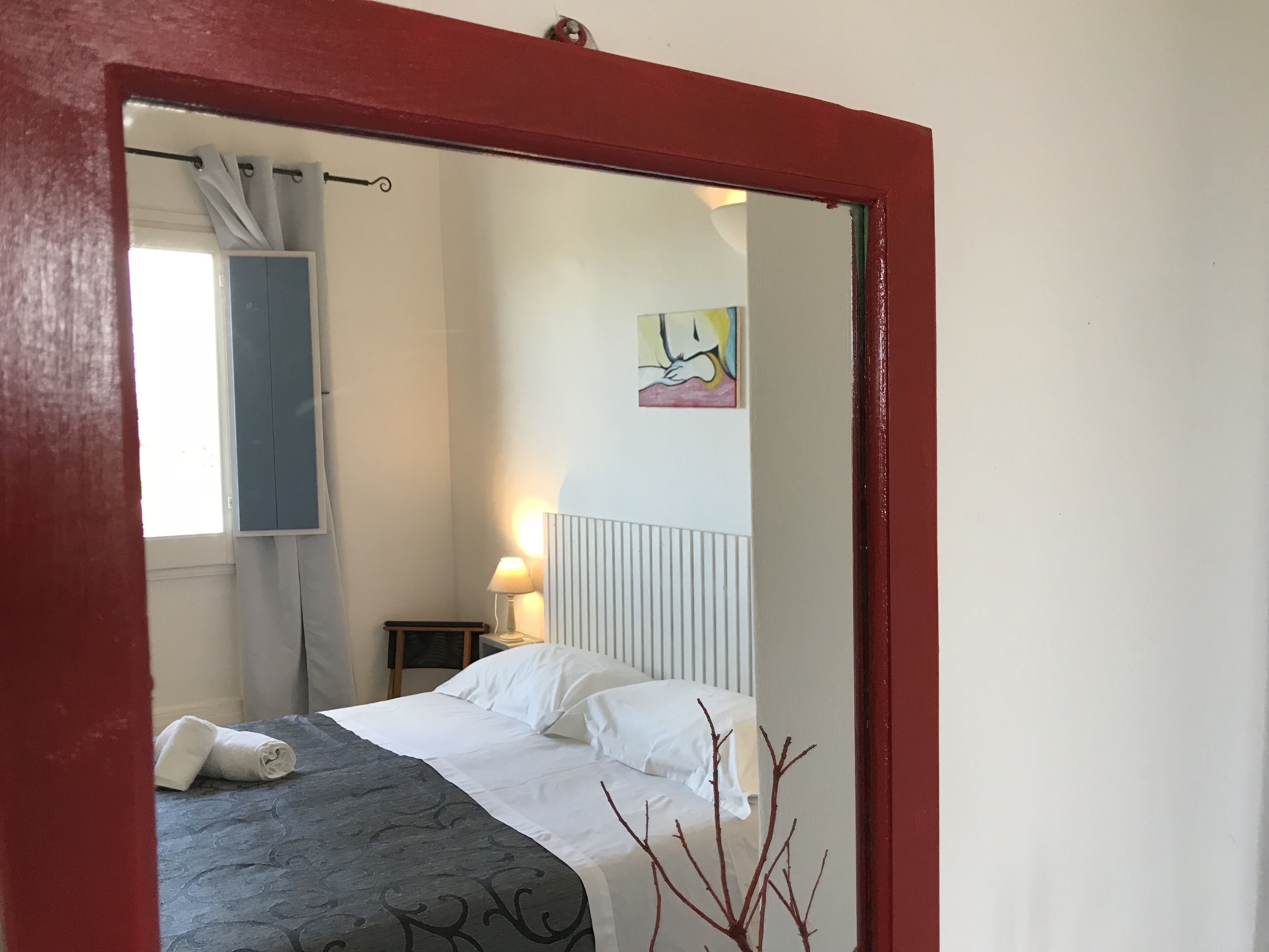 Une chambre à coucher avec un lit, une table de chevet, une lampe, un tableau et une fenêtre avec des rideaux.