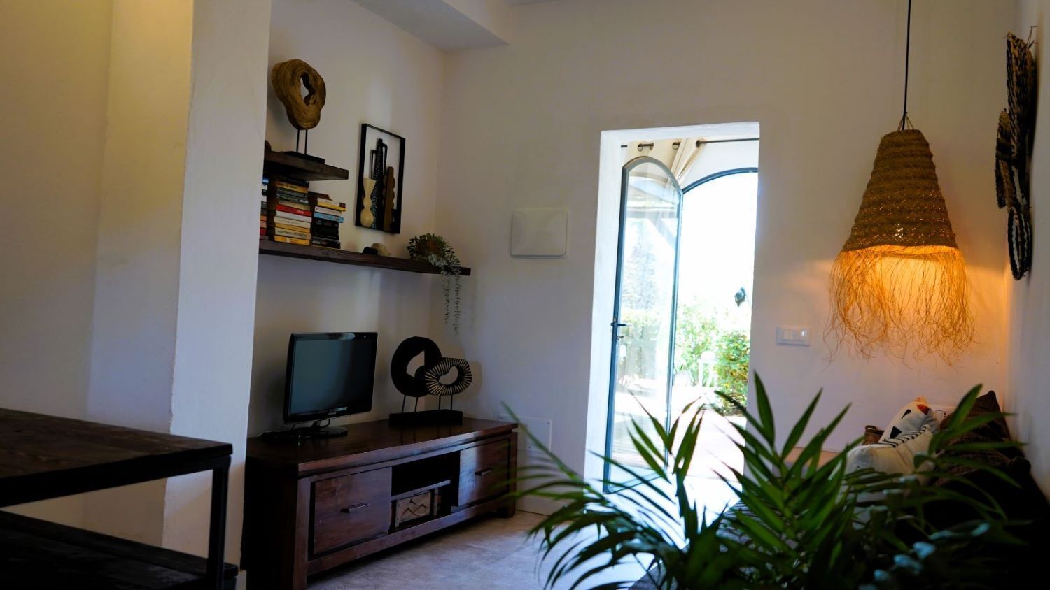 Sala de estar com televisão sobre um suporte de madeira, estante e luminária pendente.