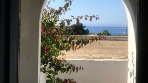 Vista a través de un ventanal arqueado de un paisaje costero, con cielo despejado y una vista distante del mar.
