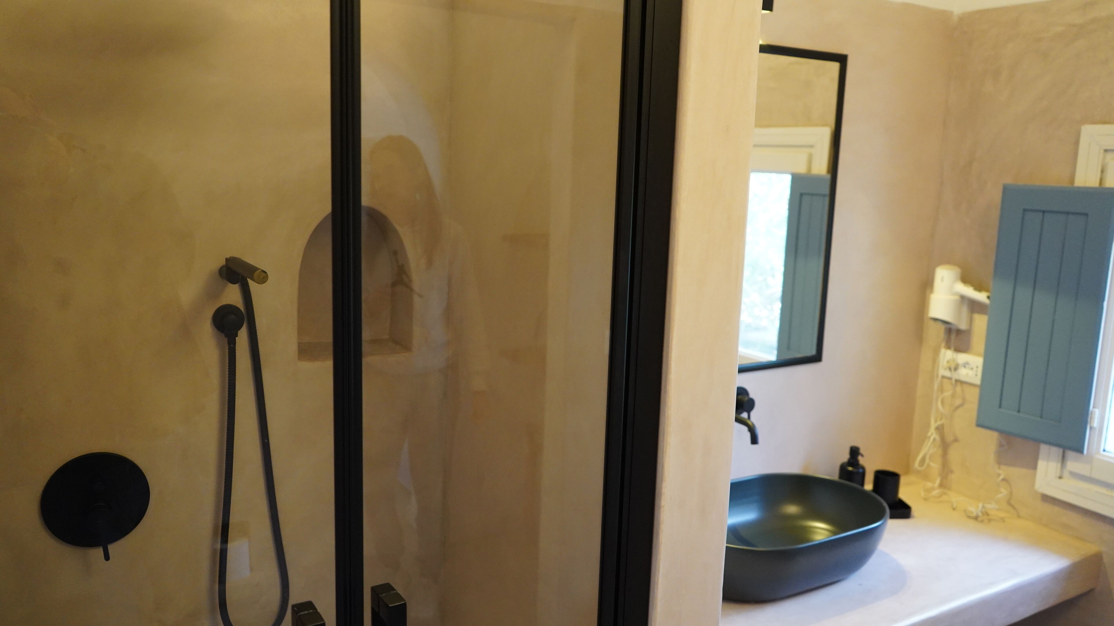 Un baño con cabina de ducha de vidrio, lavabo con lavamanos negro y espejo con mueble azul.