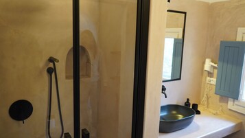 Un baño con cabina de ducha de vidrio, lavabo con lavamanos negro y espejo con mueble azul.