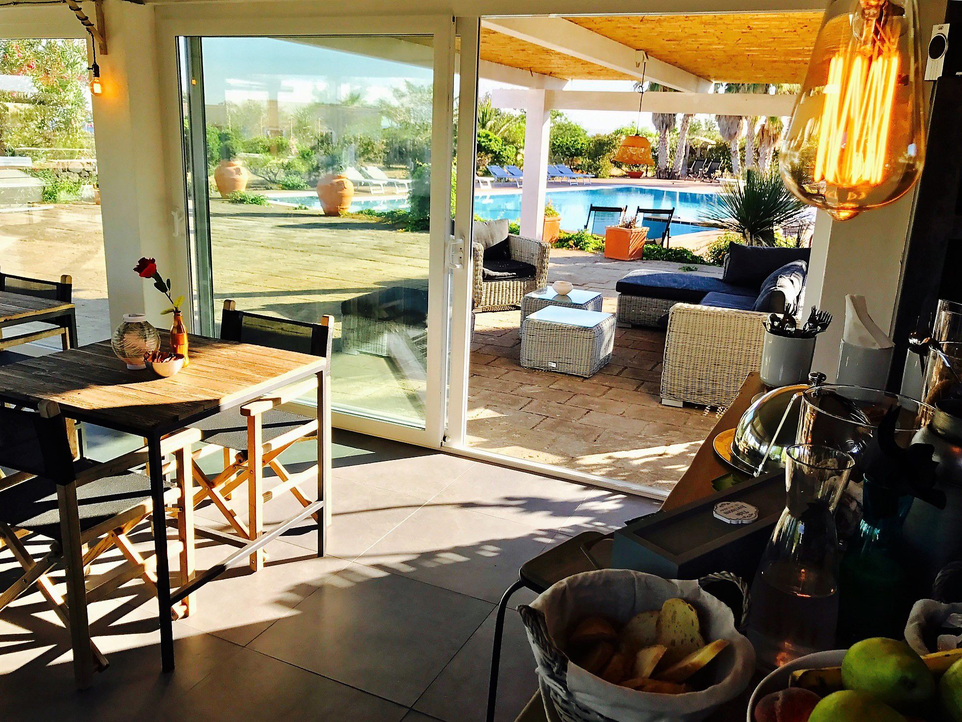 A sunlit patio with a pool view, wicker furniture, and a fruit basket.