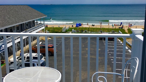 Un balcon avec vue sur la plage et l’océan. On y trouve une table et une chaise avec un coussin bleu.