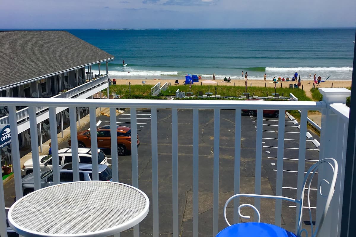 Balcón con vista a la playa y al océano. Hay una mesa y una silla con un cojín azul.