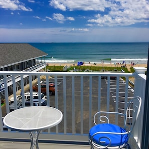 A balcony with a view of the beach and ocean. There is a table and a chair with a blue cushion. - The Rebekah Inn (Old Orchard Beach)