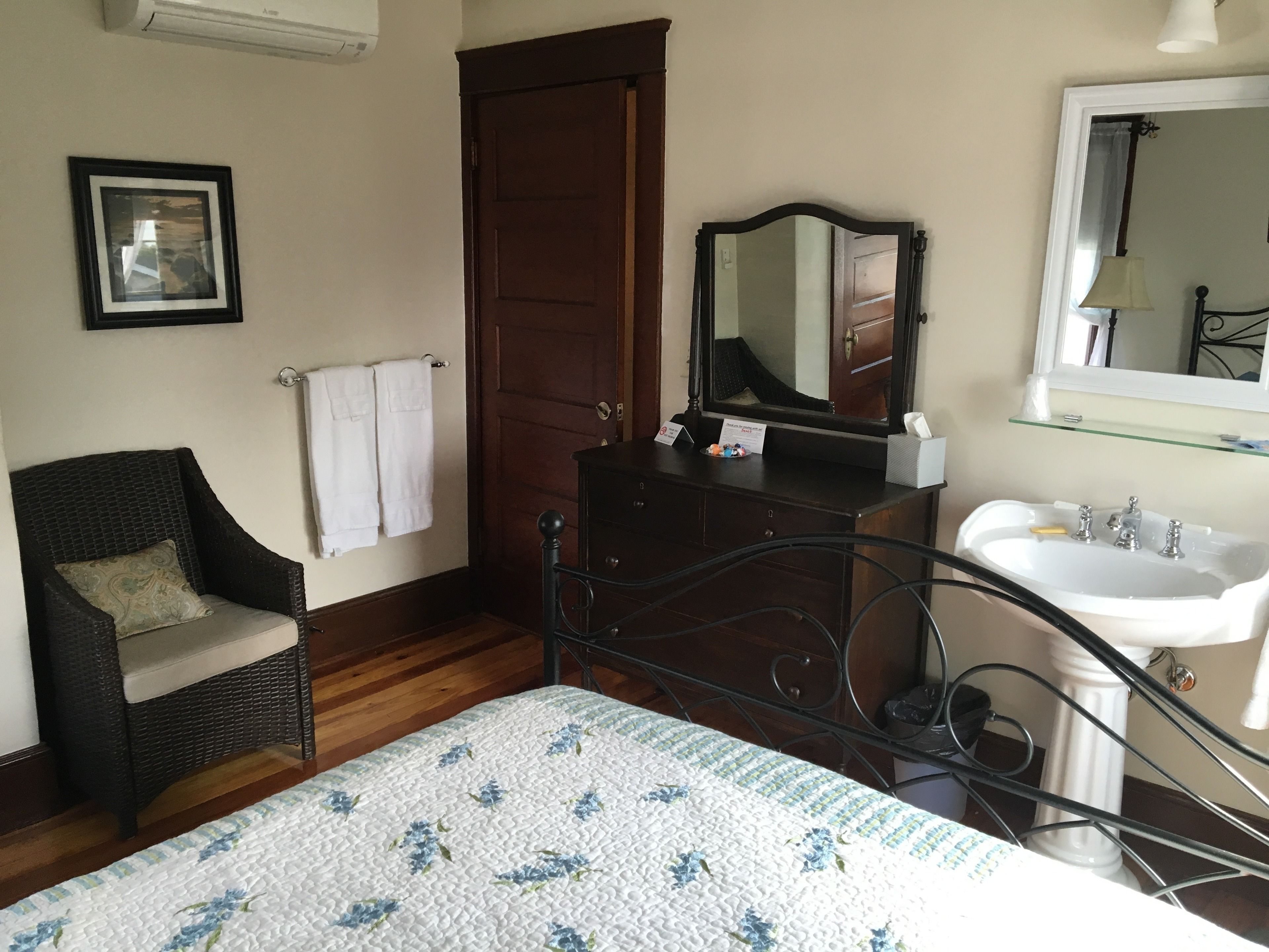 A bedroom with a bed, a chair, a dresser, a mirror, and a bathroom with a sink.