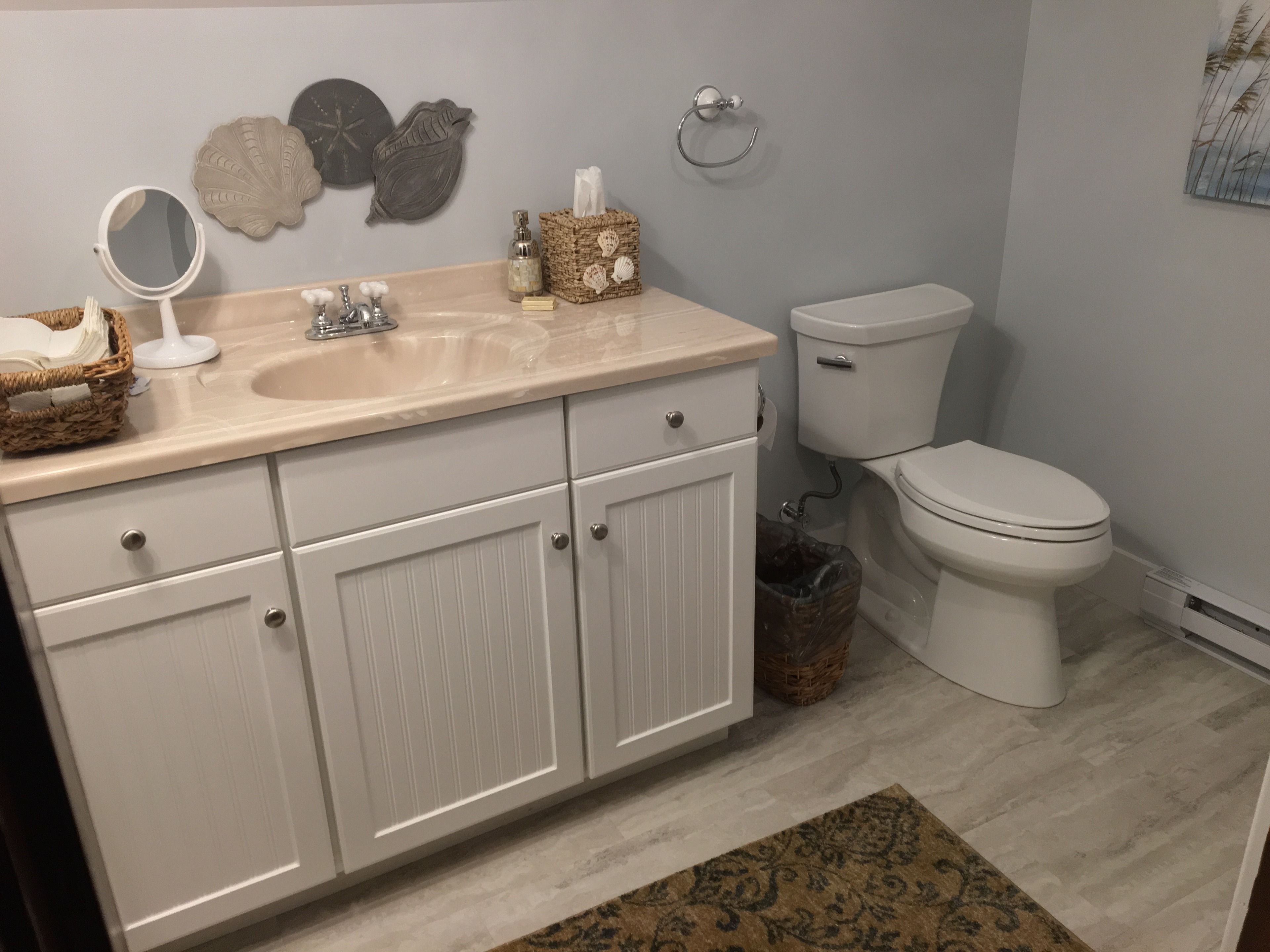 Et badeværelse med en beige vask, hvide skabe, et toilet og dekorative skaller på væggen.