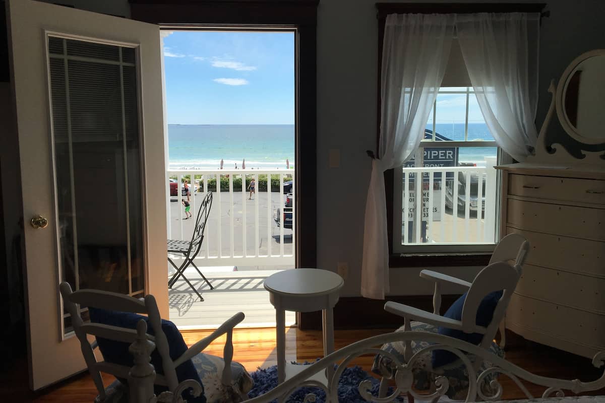 Una habitación con vistas a la playa, un balcón con una silla y una mesa, y un aparador.