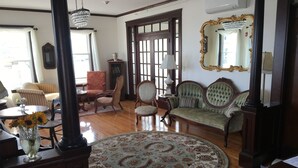 Une pièce avec un tapis rond à motifs, un canapé vert, un fauteuil rouge, une table basse en bois et un vase rempli de tournesols.