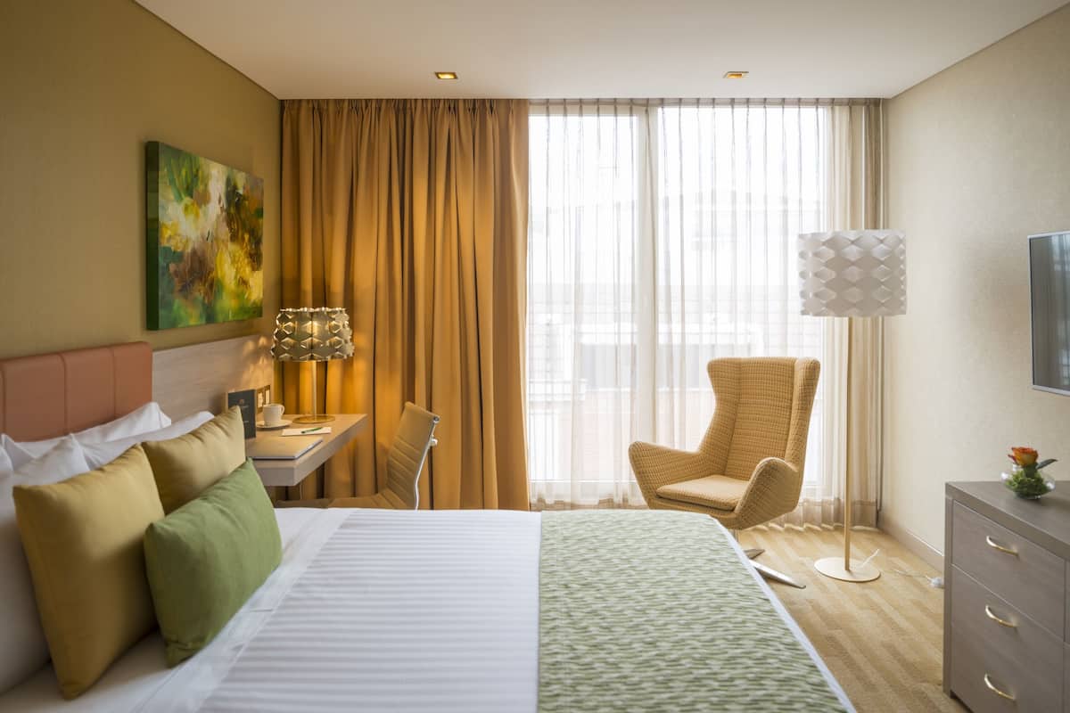 A hotel room with a bed, a desk, a chair, a TV, and a window with curtains.