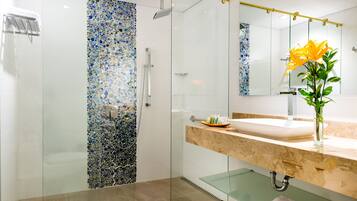 Une salle de bain moderne avec une douche en verre, des toilettes blanches, un lavabo en marbre et un miroir agrémenté d’un vase de fleurs.