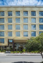 Un hotel con fachada geométrica, múltiples ventanas y un área de entrada bien cuidada con plantas en macetas.