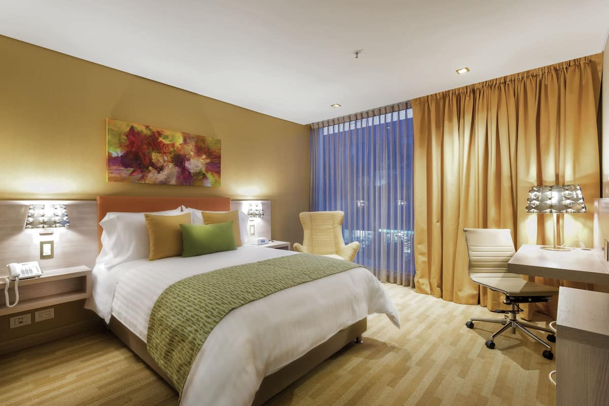 A hotel room with a bed, a desk, a chair, and a window with curtains.