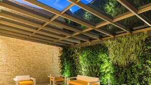 An indoor patio with a glass ceiling, wooden benches, and a green wall with plants. - Hotel El Dorado Bogota (Bogotá)