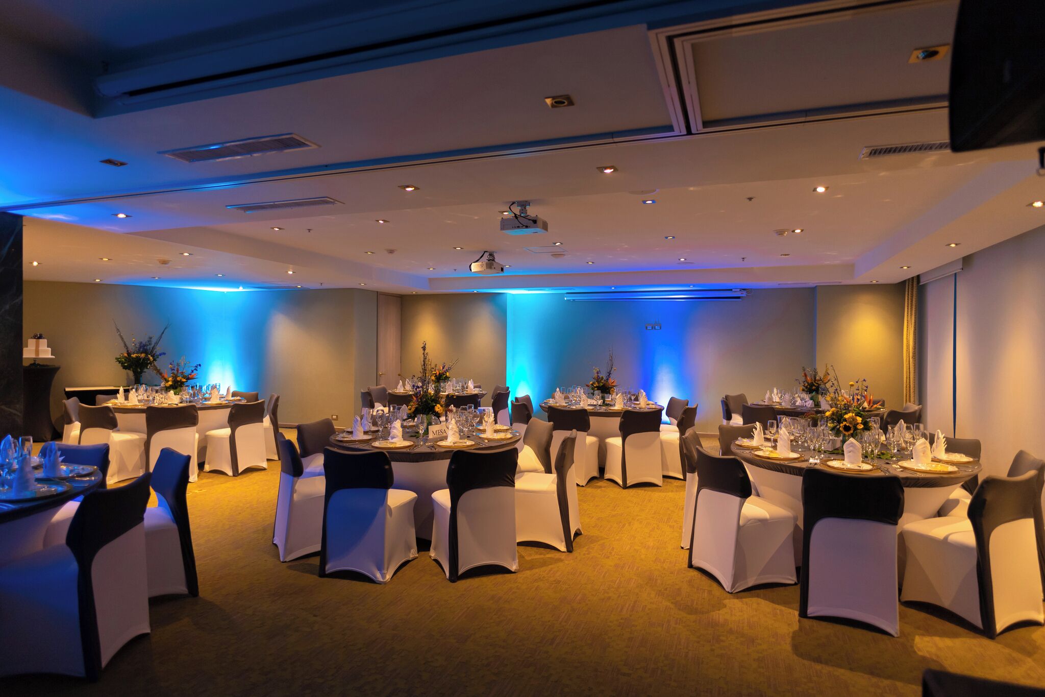 Un salón de conferencias con mesas redondas, sillas blancas e iluminación ambiental azul.